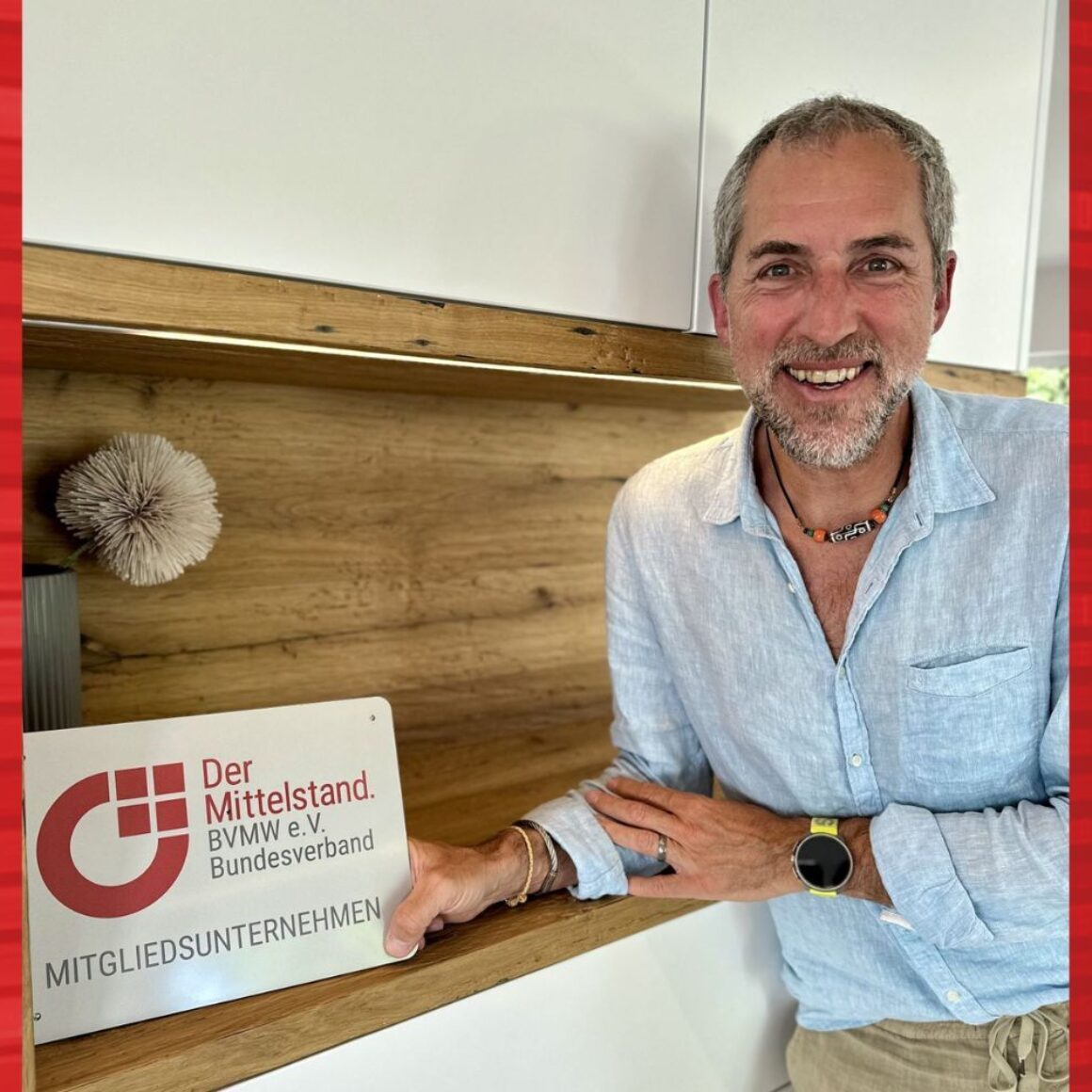 Boris Bregar mit BVMW Mitgliedsunternehmen Schild, Halbportrait, Schild in der rechten Hand